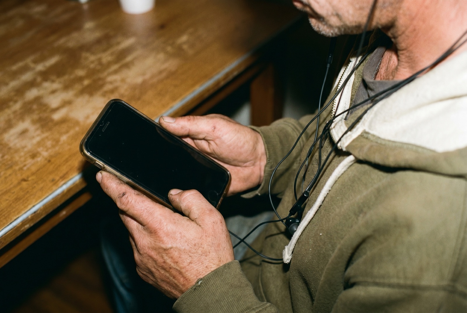 Primer plano de las manos de un Beatboxer sosteniendo un móvil, con auriculares de cable colgando del cuello