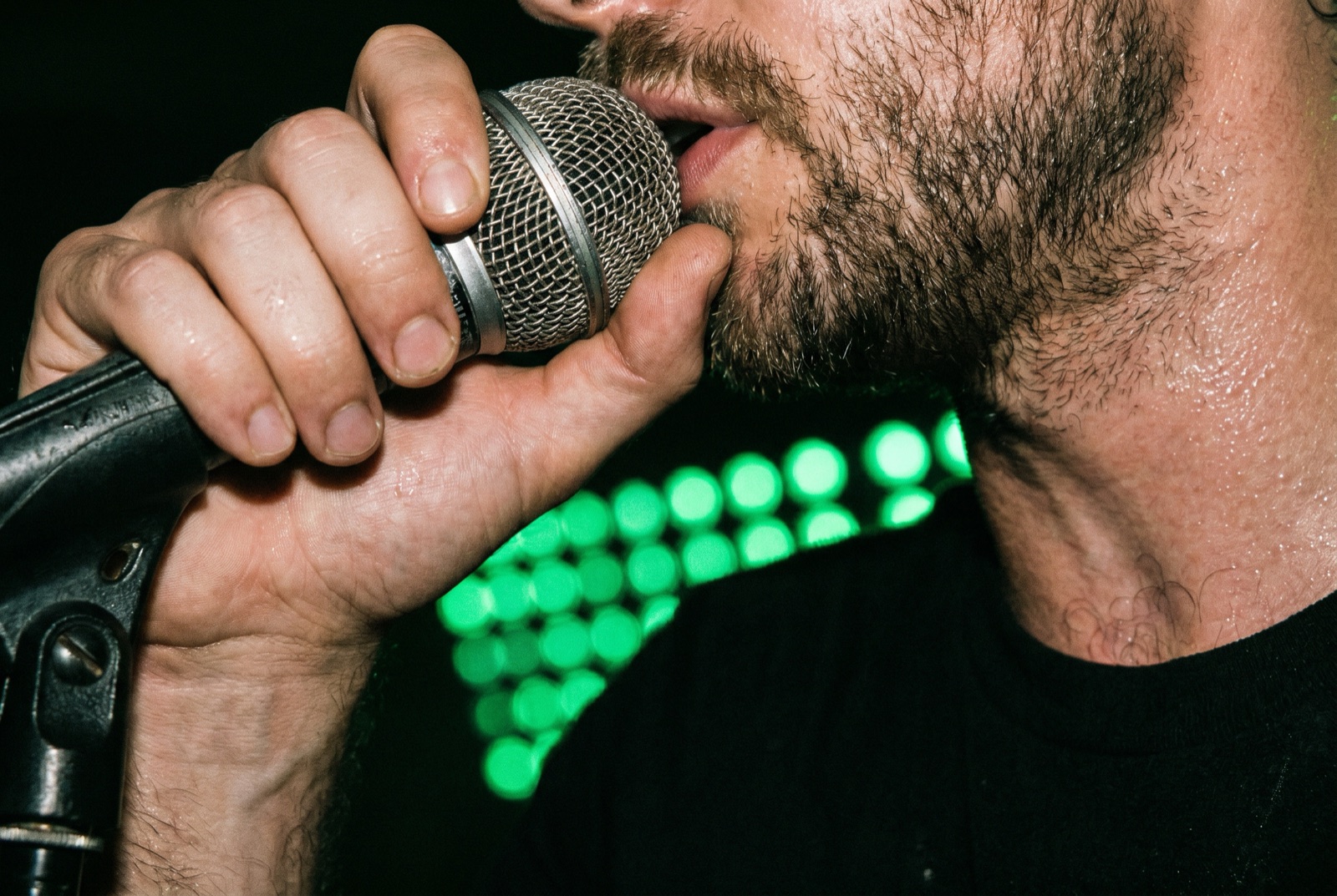 Un Beatboxer agarrando un micrófono en plena actuación bajo una intensa luz verde de escenario